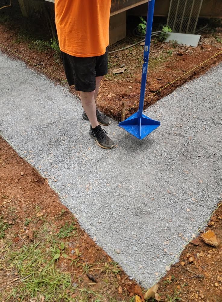 Person in orange shirt holding a blue tool on a newly poured concrete path.