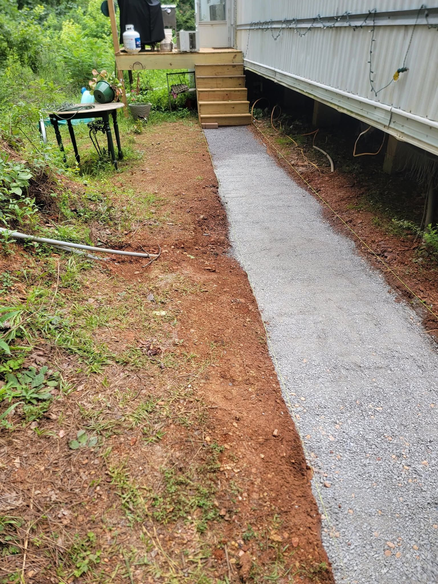 Gravel path beside a house, with wooden steps and a small table in a grassy yard.