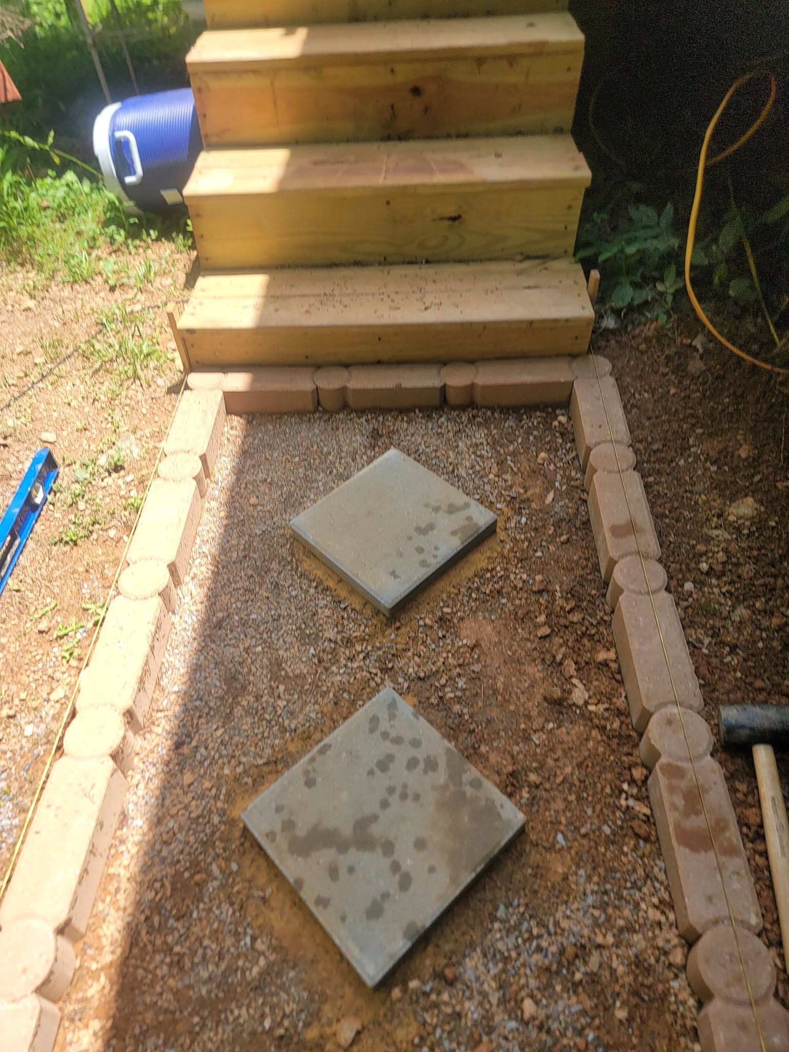Outdoor steps above a gravel path with two square stepping stones and a small utility cover below