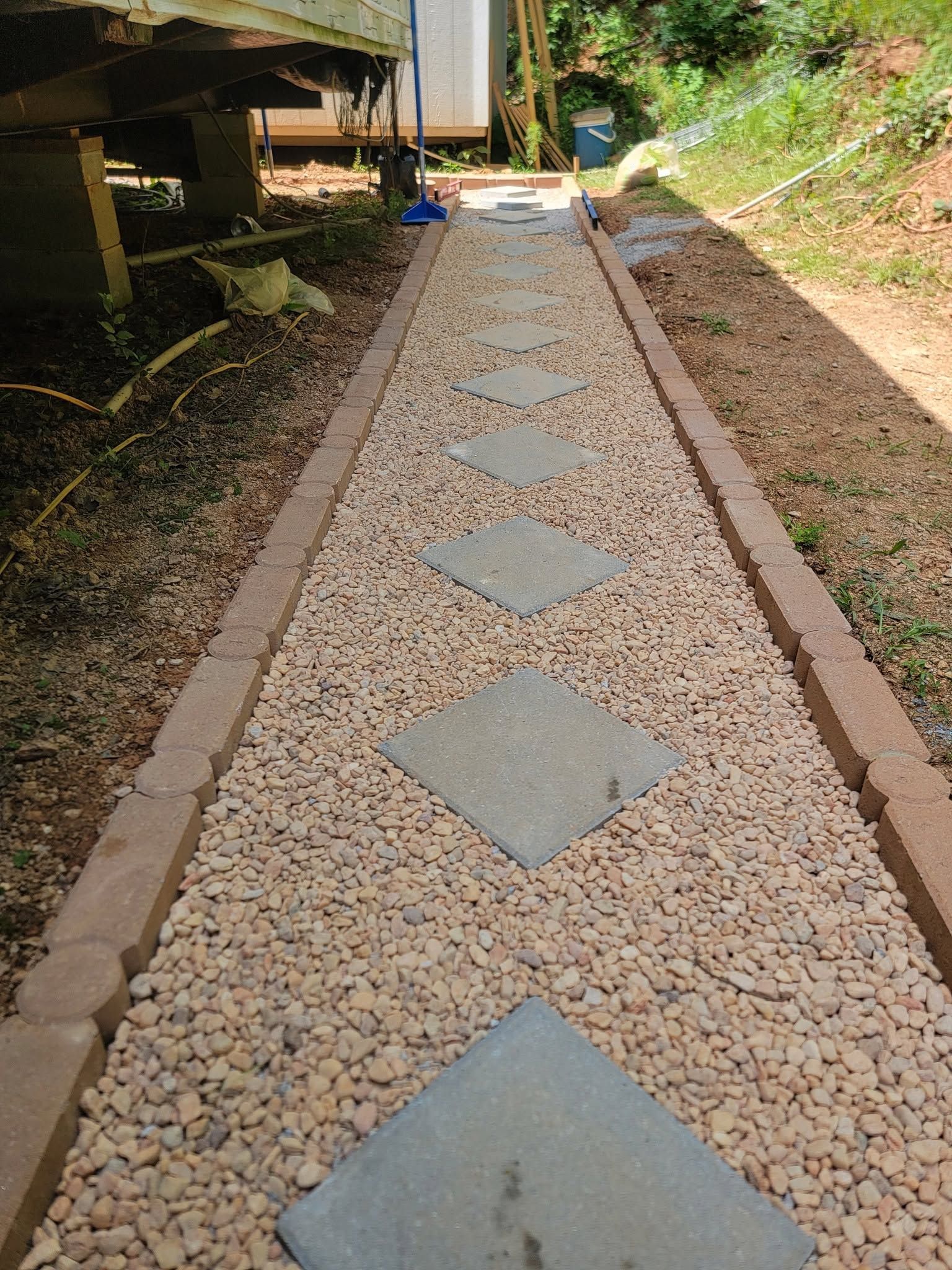 Gravel walkway with large square stepping stones between low retaining walls outdoors.