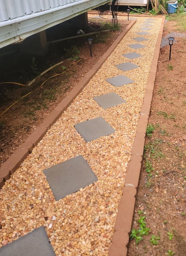 Gravel walkway with stepping stones beside a raised house foundation