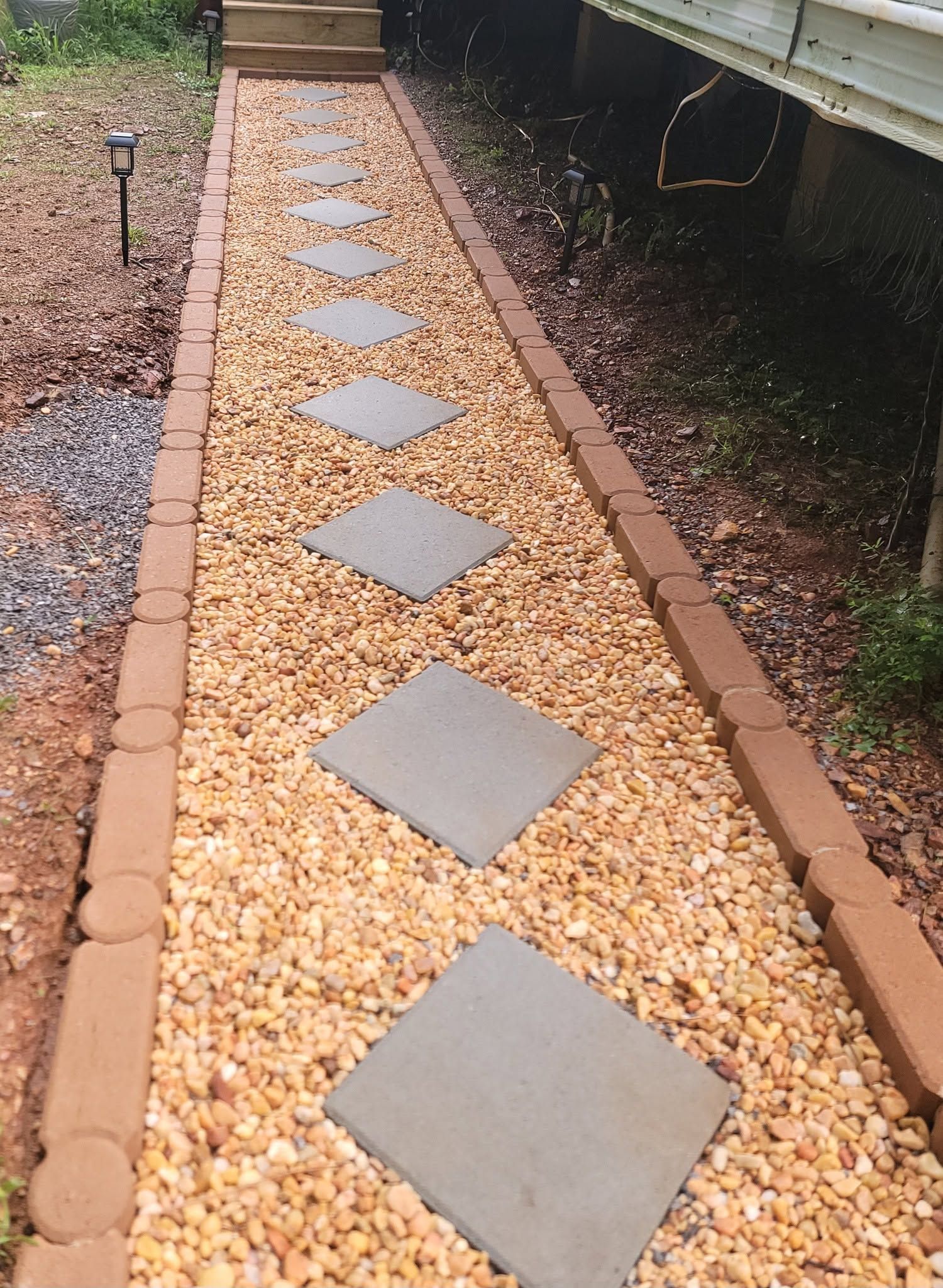 Stone walkway with gray stepping stones set in tan gravel beside a deck