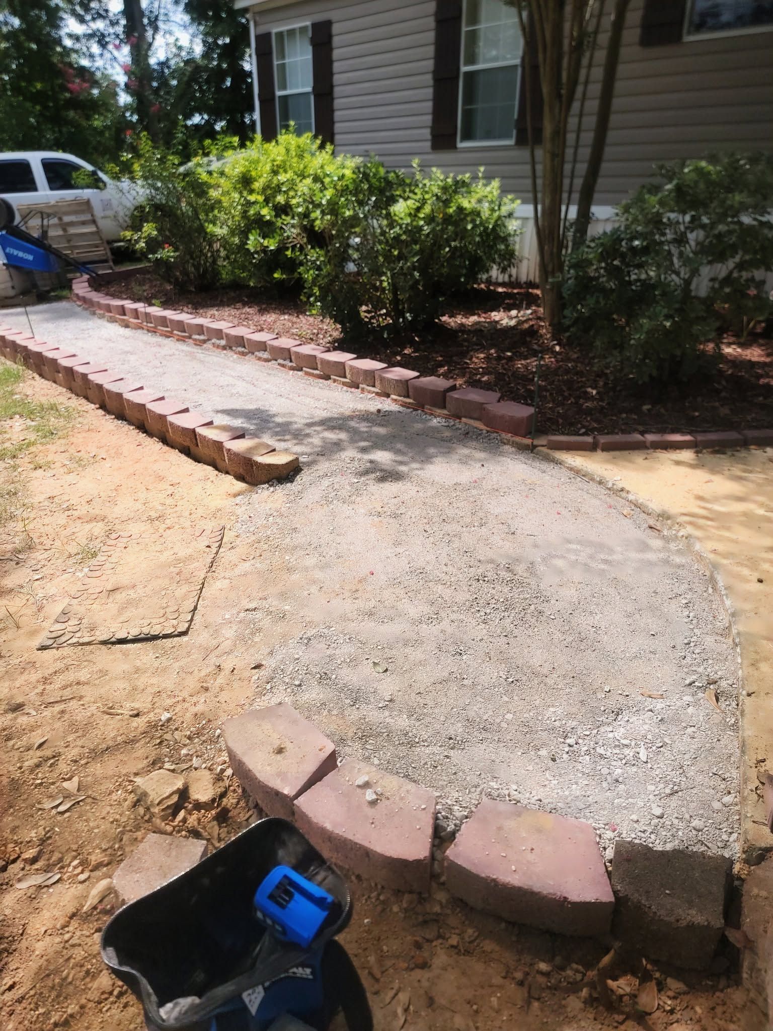 Concrete walkway under construction beside a house, with brick edging and shrubs along the border.