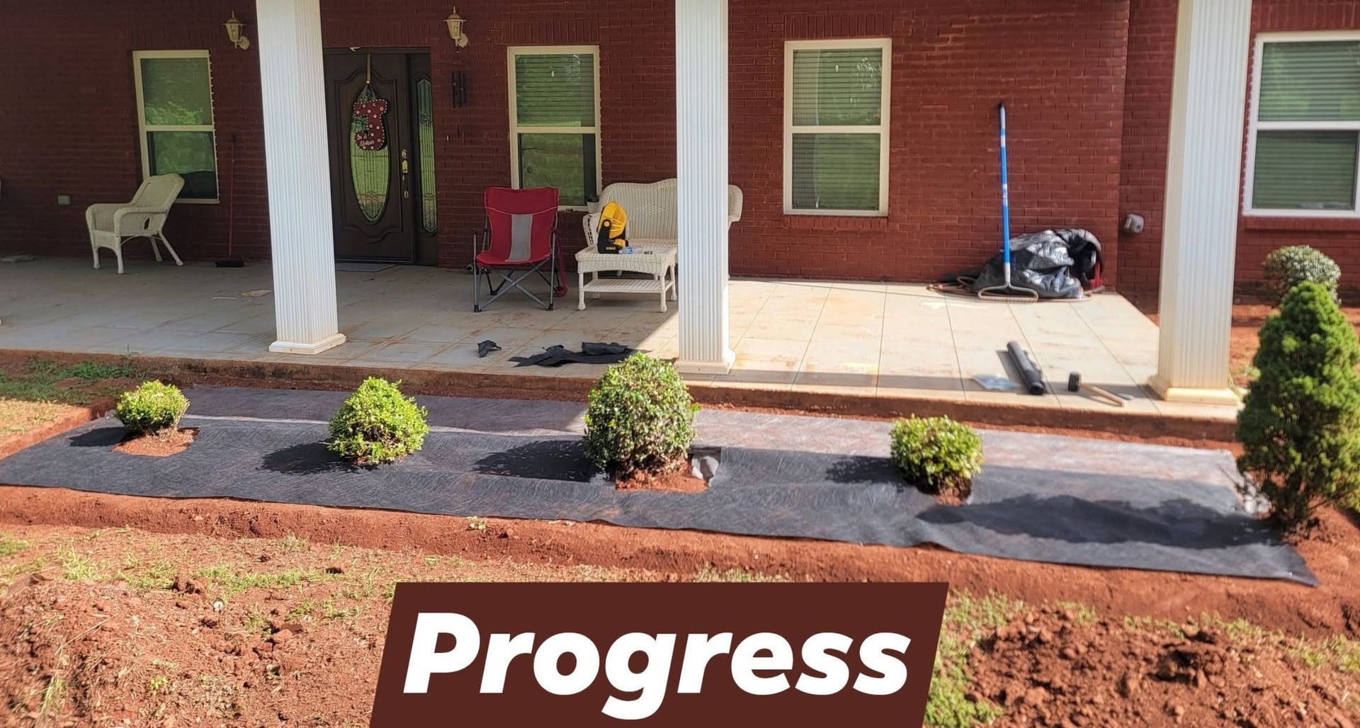 Brick house porch with chairs, new landscaping, and a “Progress” sign in front