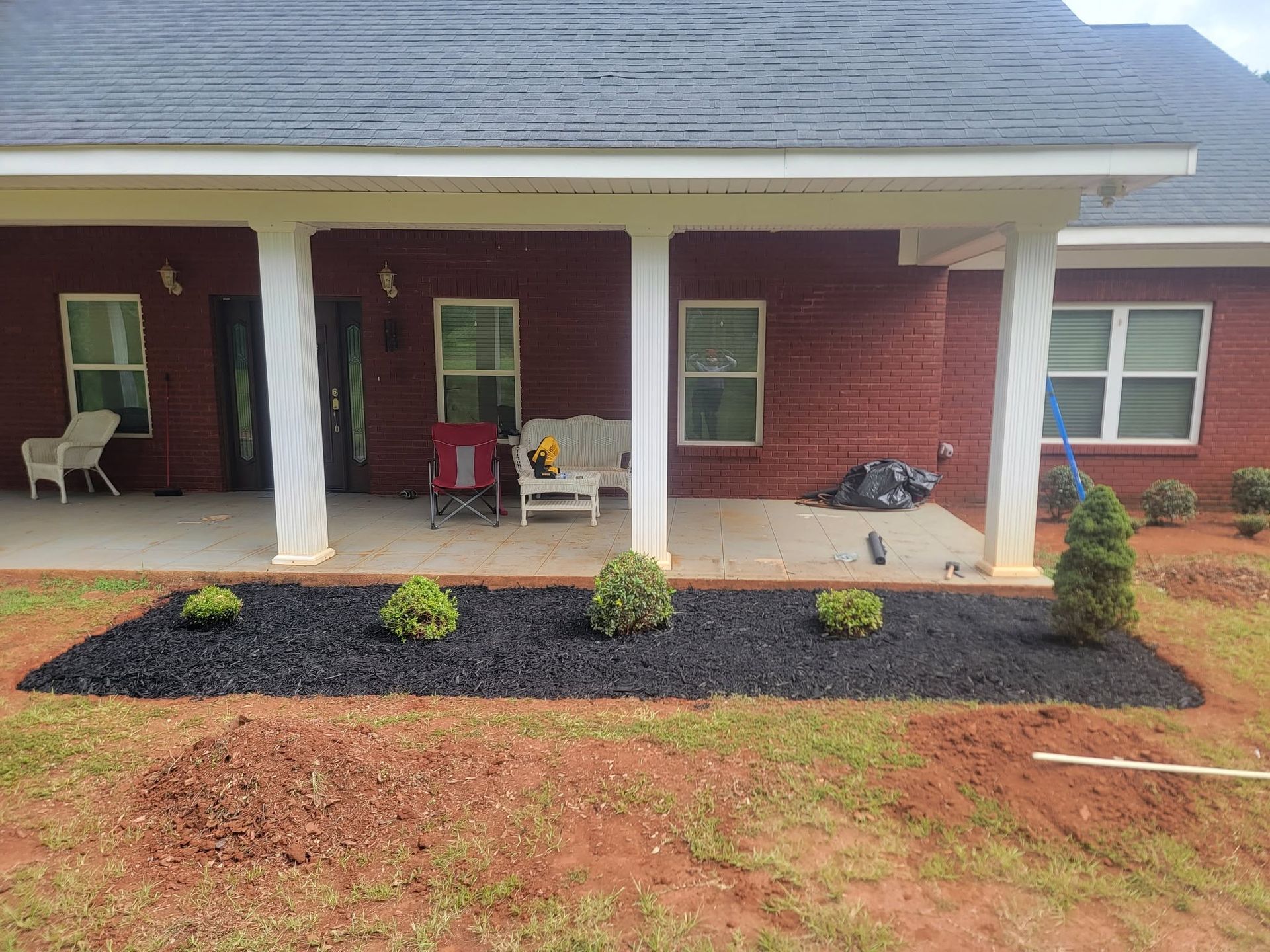 Front porch of a brick house with white columns and a mulched flower bed in front