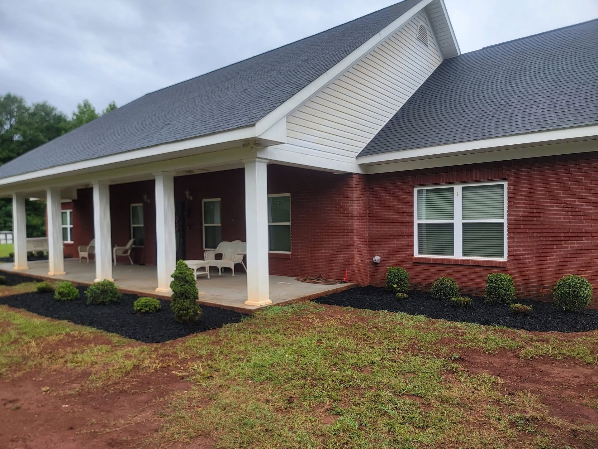 Red brick house with white porch columns, gray roof, and landscaped front yard