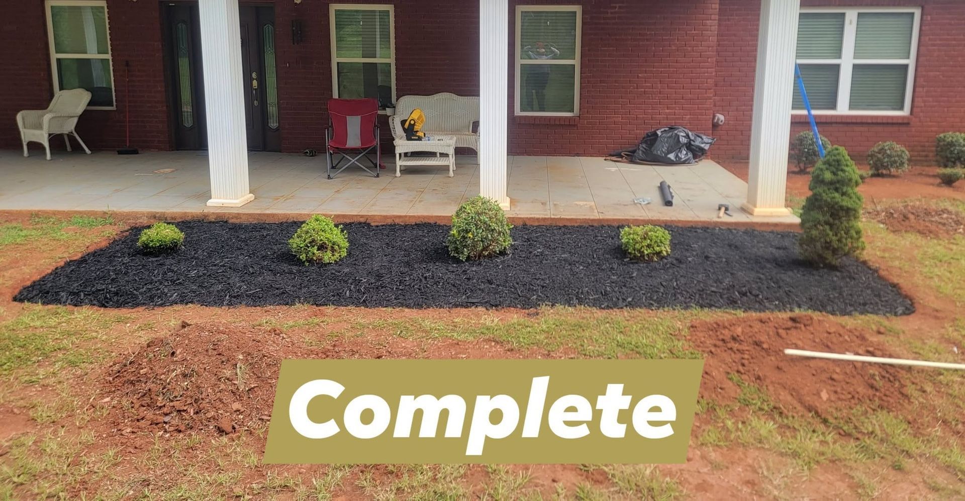 Freshly landscaped front porch with mulch bed, small shrubs, and a “Complete” sign in the yard