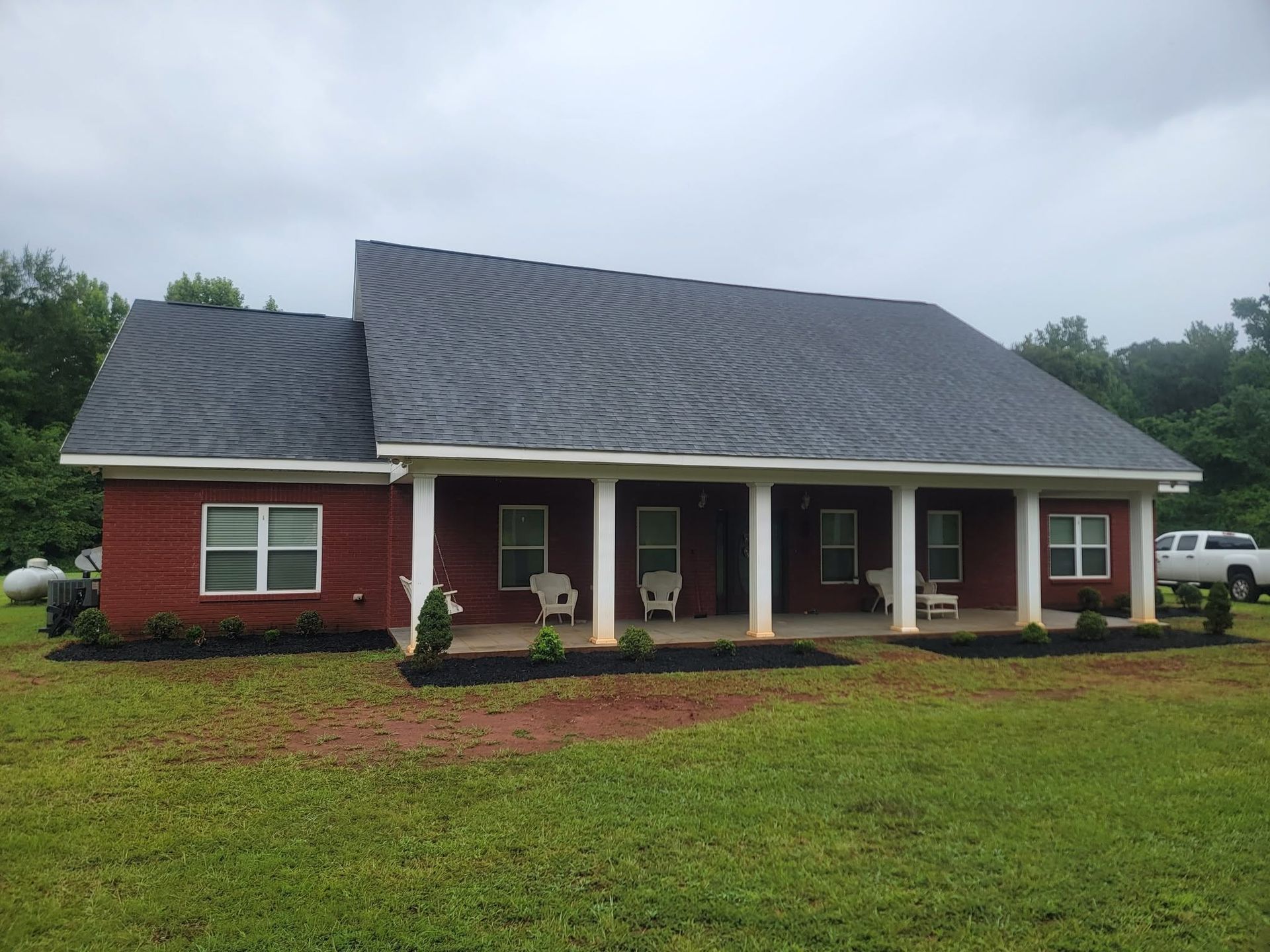 Red brick house with white columns, dark roof, and a covered front porch on a grassy lawn.