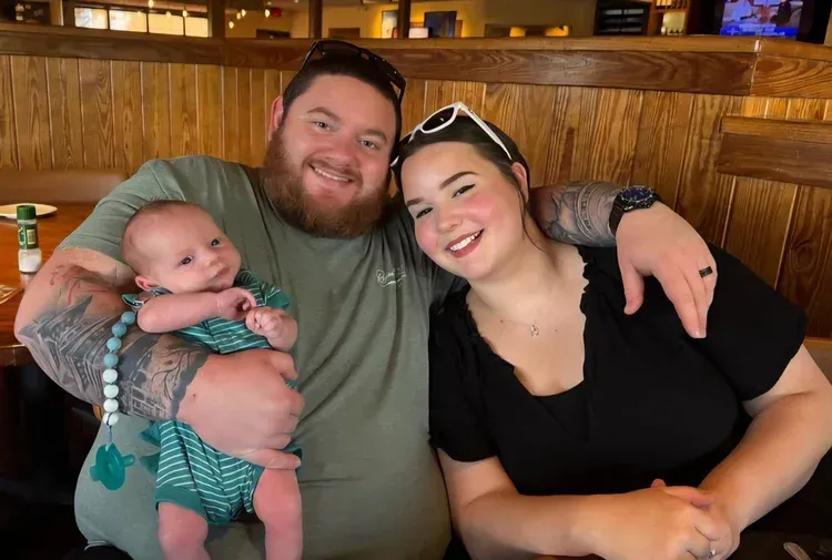 Smiling group of three on a wooden bench in a restaurant, holding a baby in green striped clothes