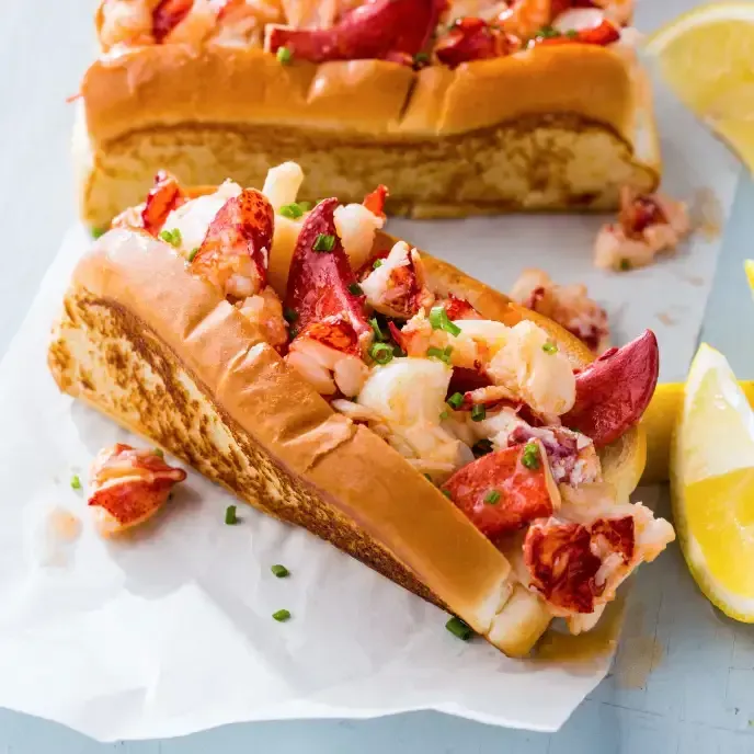 A lobster roll is sitting on a piece of paper next to lemons.