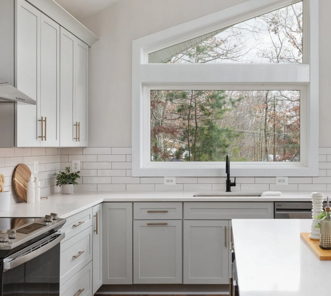 Bright modern kitchen remodel with white shaker cabinets, white countertops, subway tile backsplash, black faucet, large picture window, and natural outdoor views.