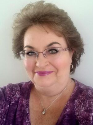 A woman wearing glasses and a purple shirt is smiling for the camera.