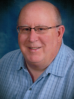 A bald man wearing glasses and a blue shirt is smiling for the camera.
