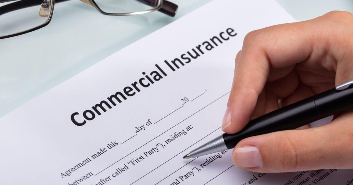 A person is signing a commercial insurance form with a pen.
