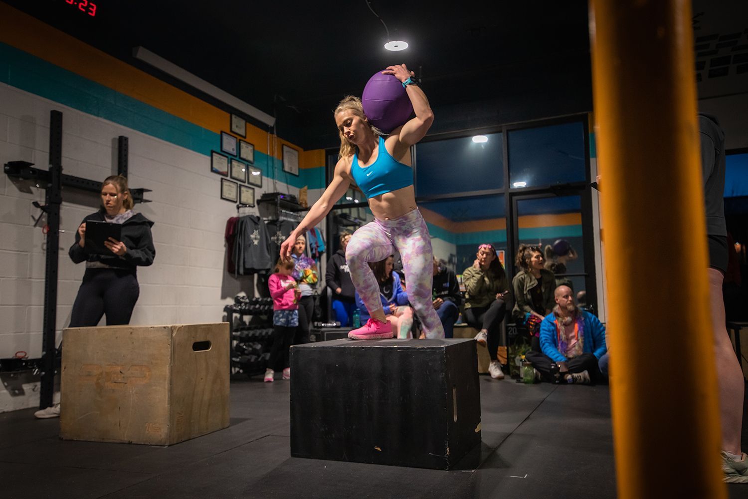 Indoor gym competition with a woman balancing on a black box while holding a purple medicine ball in Buena Vista, CO