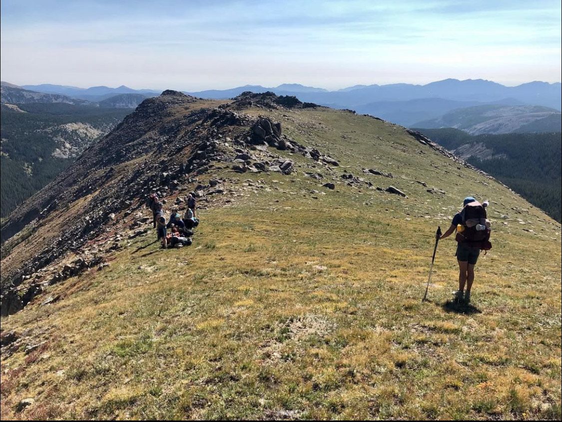 Hikers on a grassy mountain ridge with panoramic blue sky and distant peaks