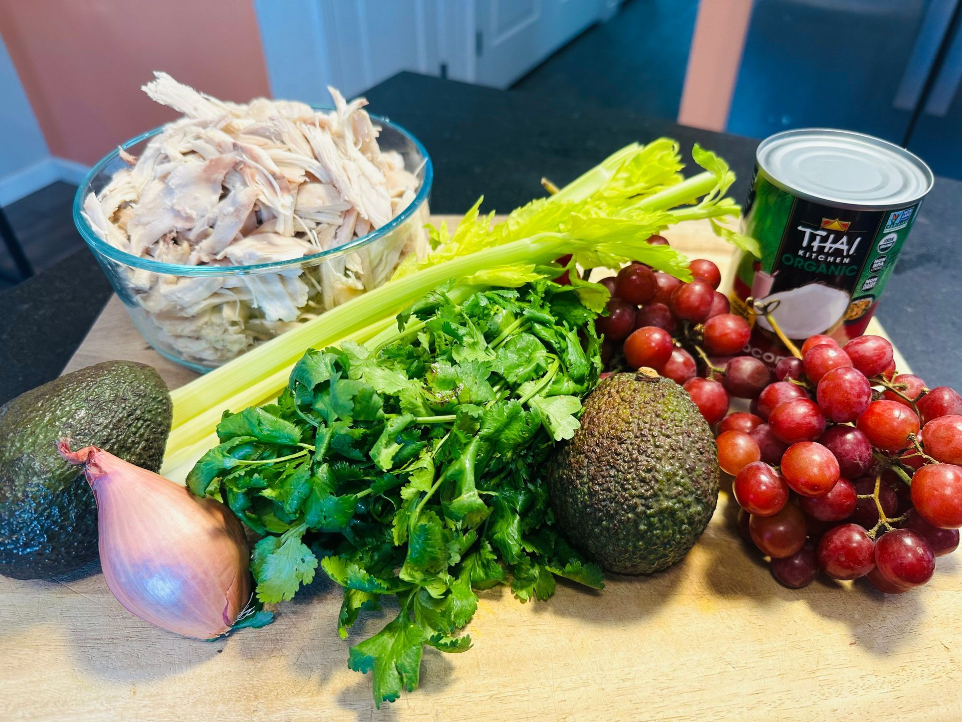 Ingredients on a counter: shredded chicken, avocado, cilantro, onions, tomatillos, tomatoes, and a can of broth