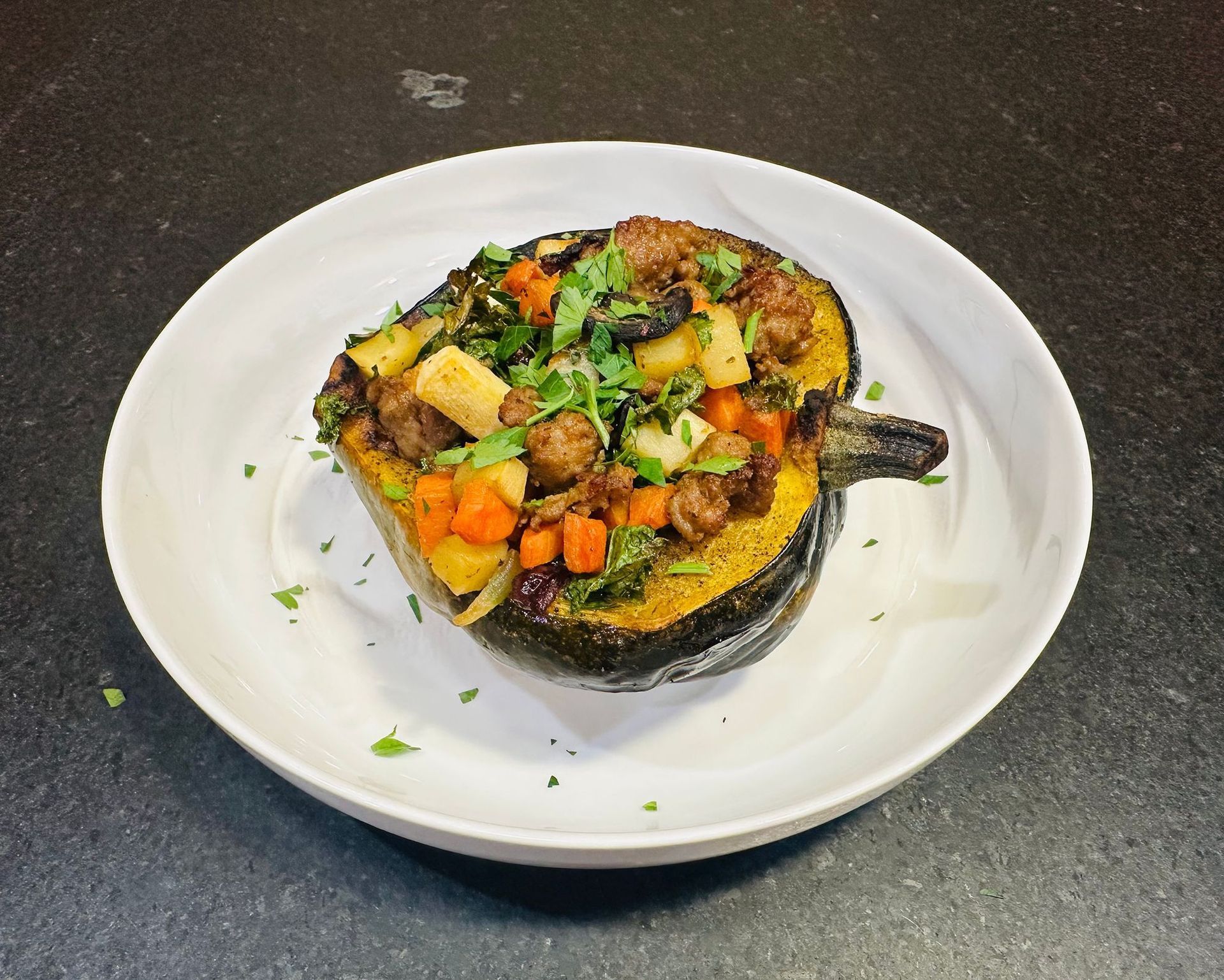 Stuffed roasted squash on a white plate, topped with mixed vegetables and herbs.