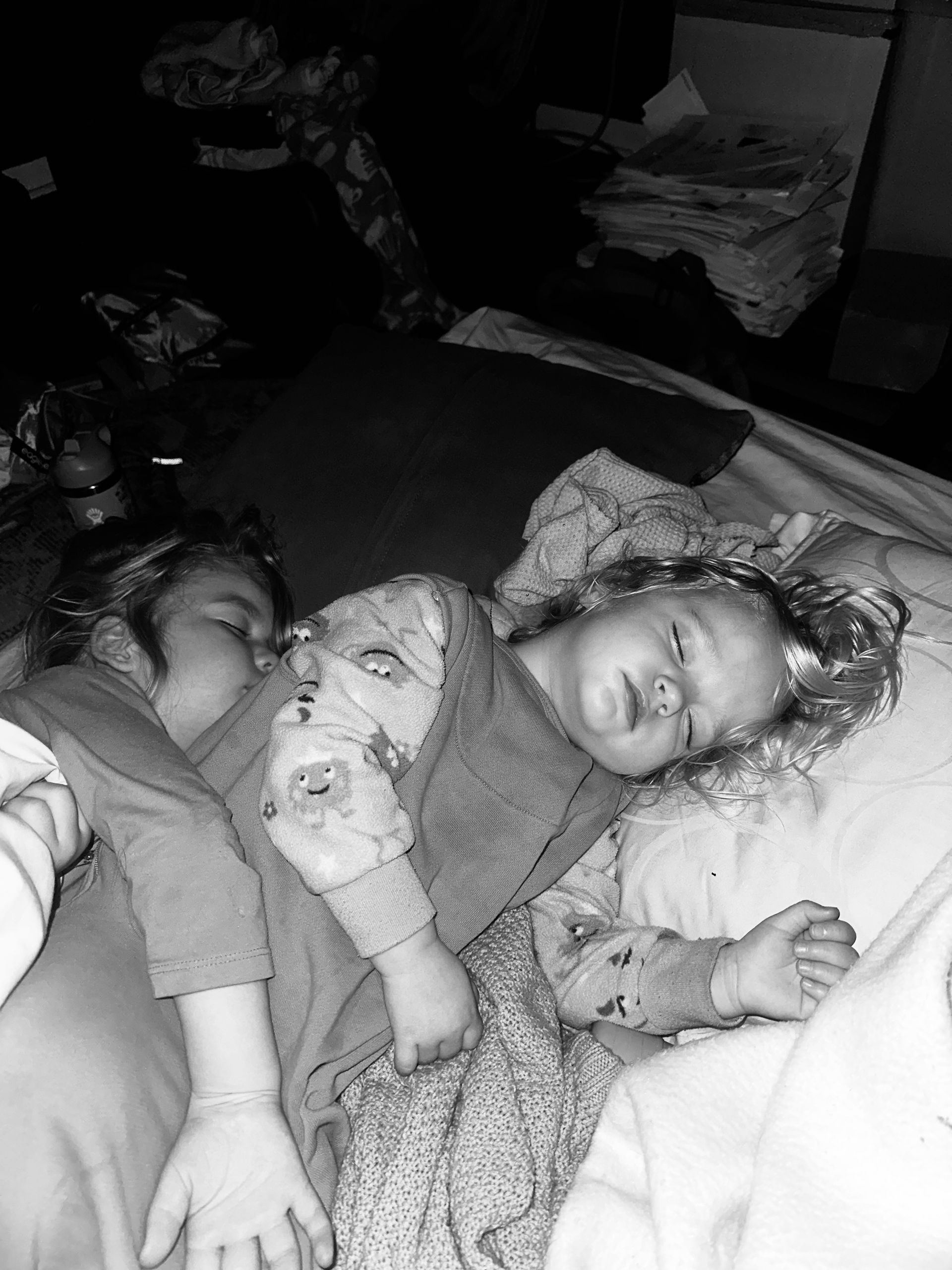 Two sleeping children lying under blankets on a bed, one holding a stuffed toy