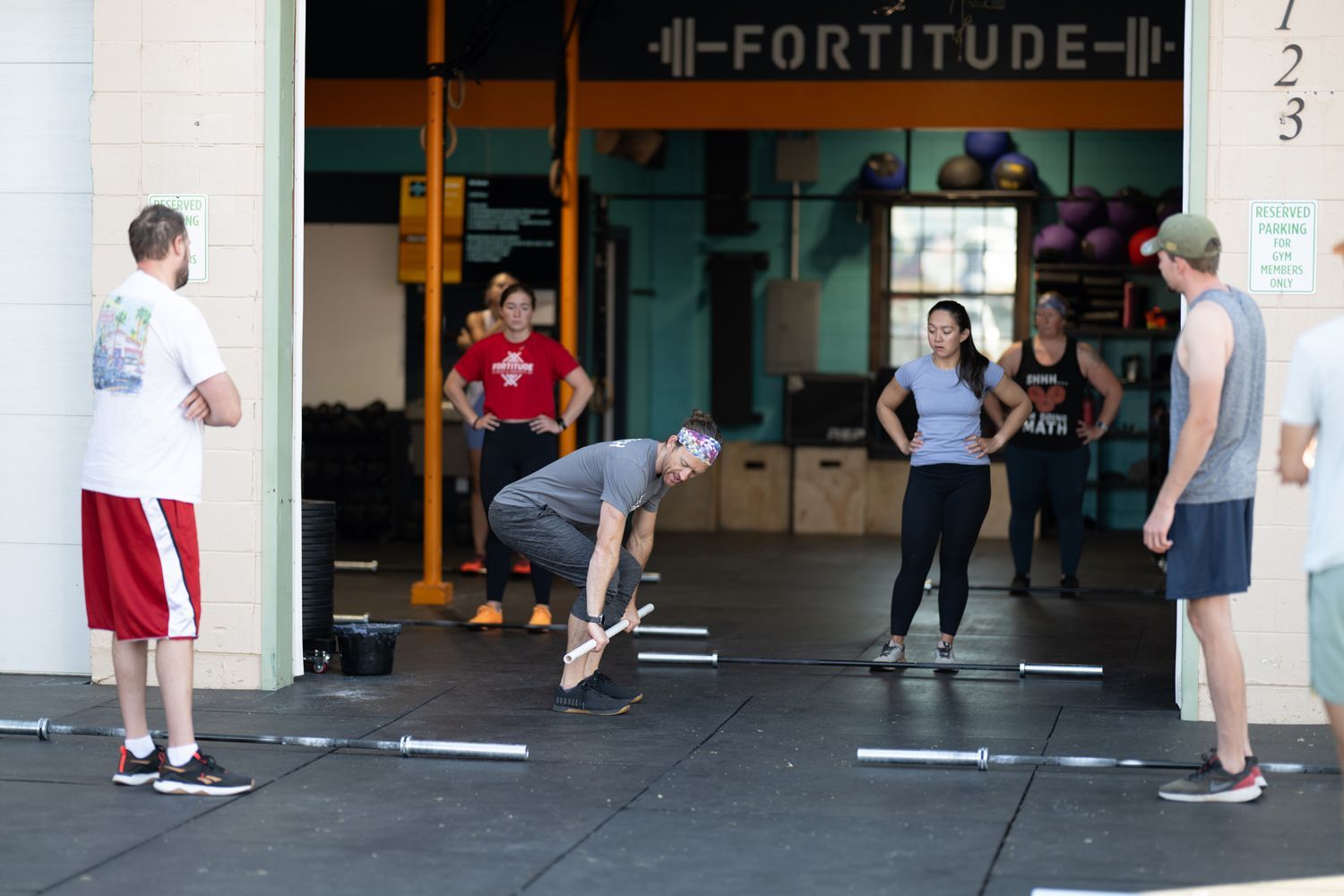 People exercising at Fortitude Fitness, with one person lifting a dumbbell and others standing nearby.