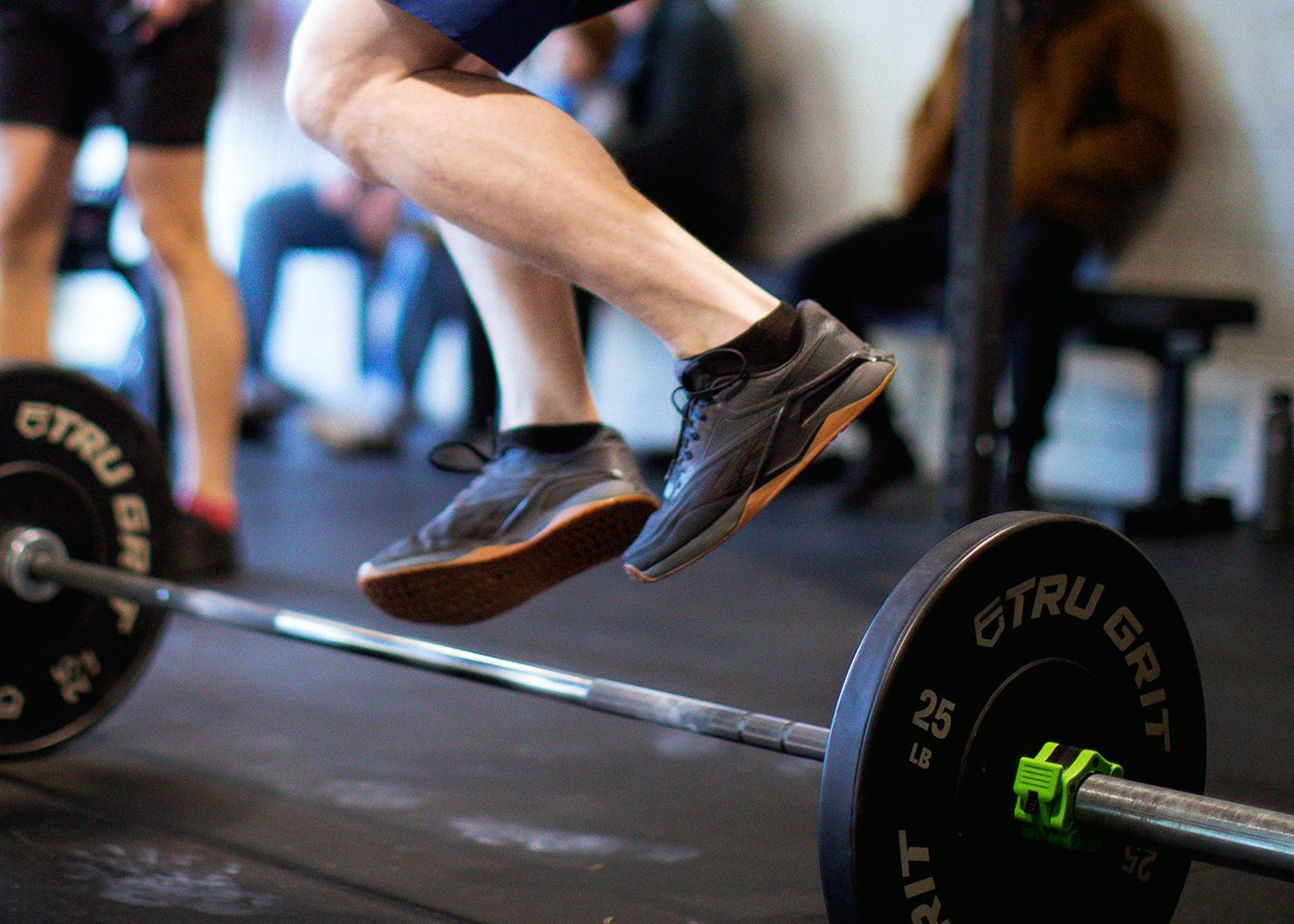 Athlete wearing Reebok Nano training shoes jumping over a barbell during a CrossFit workout.