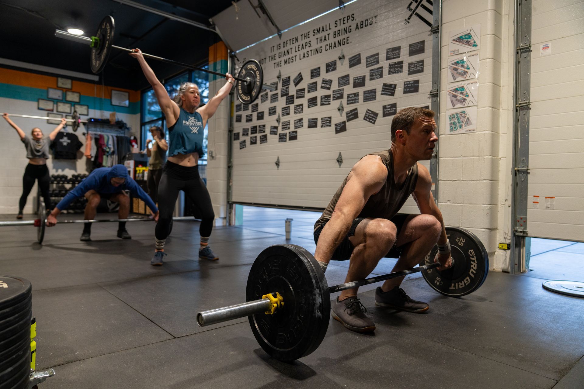 CrossFit athletes lifting barbells in a gym in Buena Vista, CO, with one woman raising weights overhead.