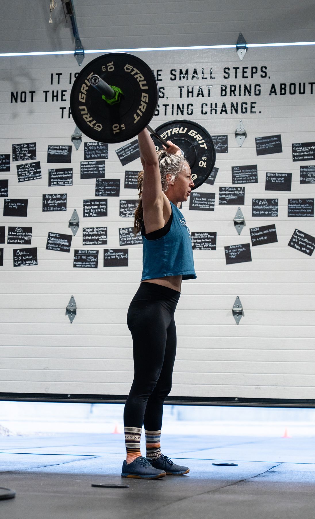 Woman lifting a barbell overhead in a gym in Buena Vista, CO, with motivational wall text behind her.