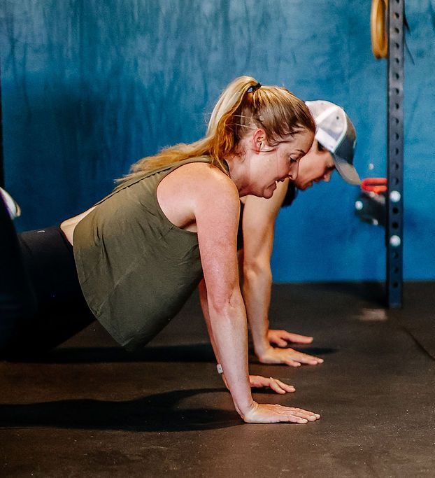 Two people doing push-ups on gym mats, with a blue wall in the background at Fortitude Fitness in Buena Vista, CO