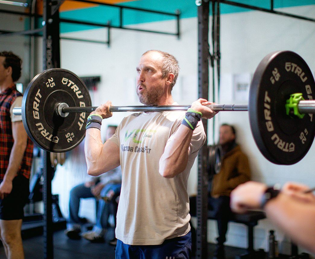 Person lifting a barbell in a gym in Buena Vista, CO, surrounded by workout equipment and blurred onlookers.