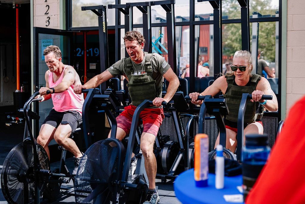 People exercising on stationary bikes in a gym, with one person in pink and others in dark colors at Fortitude Fitness