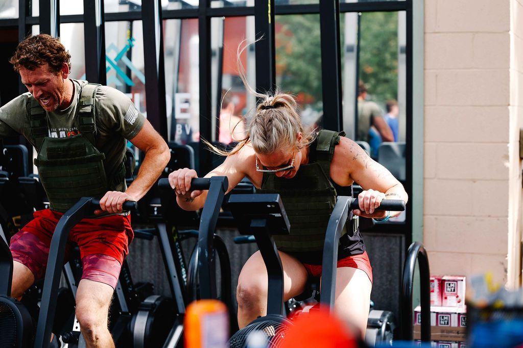 Two people exercising on stationary bikes in a gym in Buena Vista, CO, leaning forward and pedaling hard.
