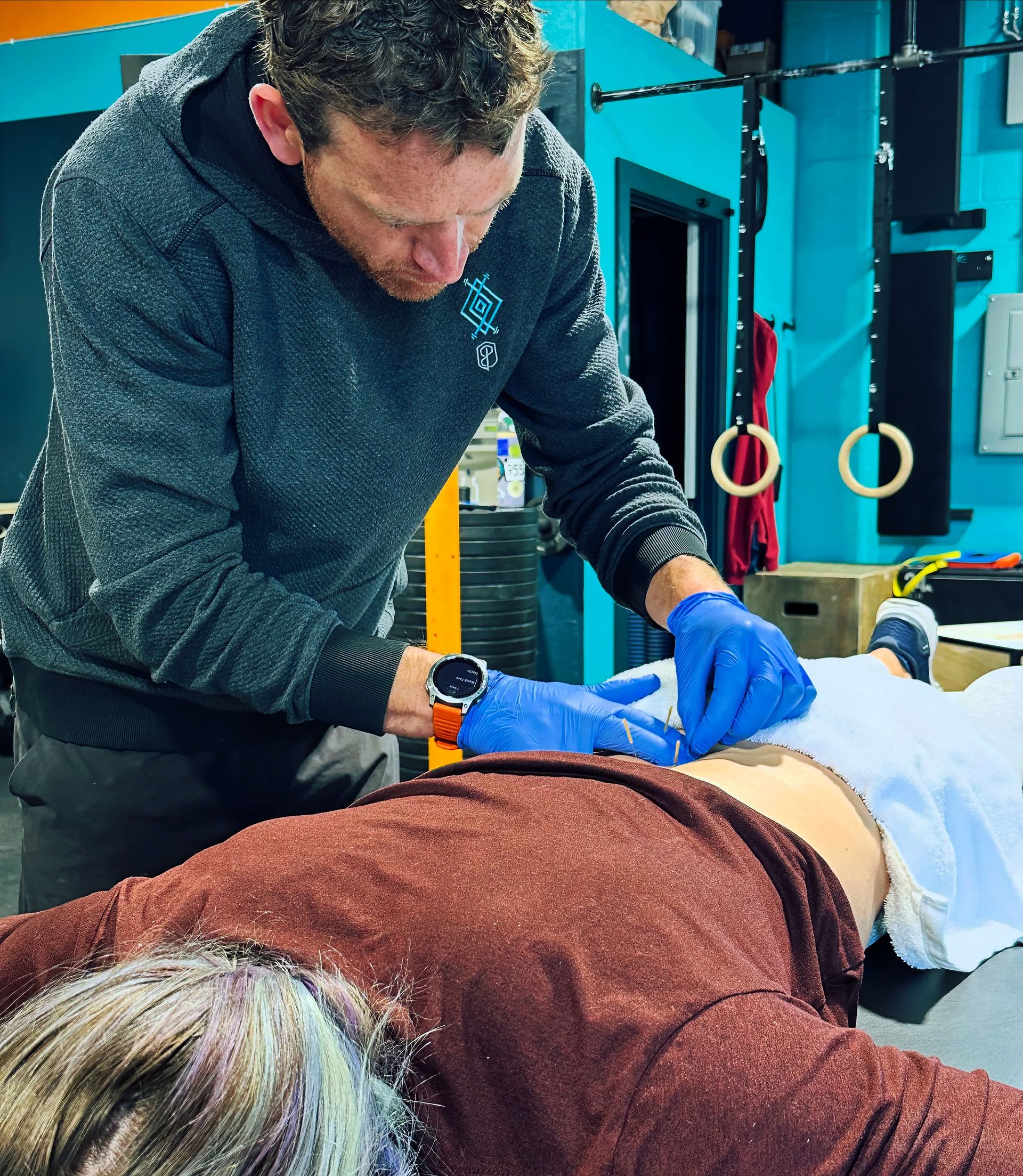 Trainer assisting a person on a table in a gym, wearing blue gloves and adjusting their back