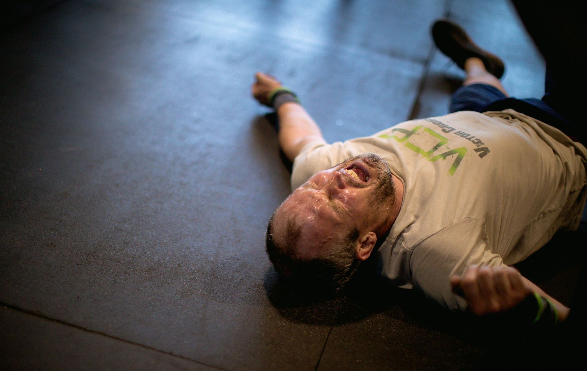 Man lying on a gym floor, arms spread out, wearing a beige shirt and dark pants at Fortitude Fitness in Buena Vista, CO
