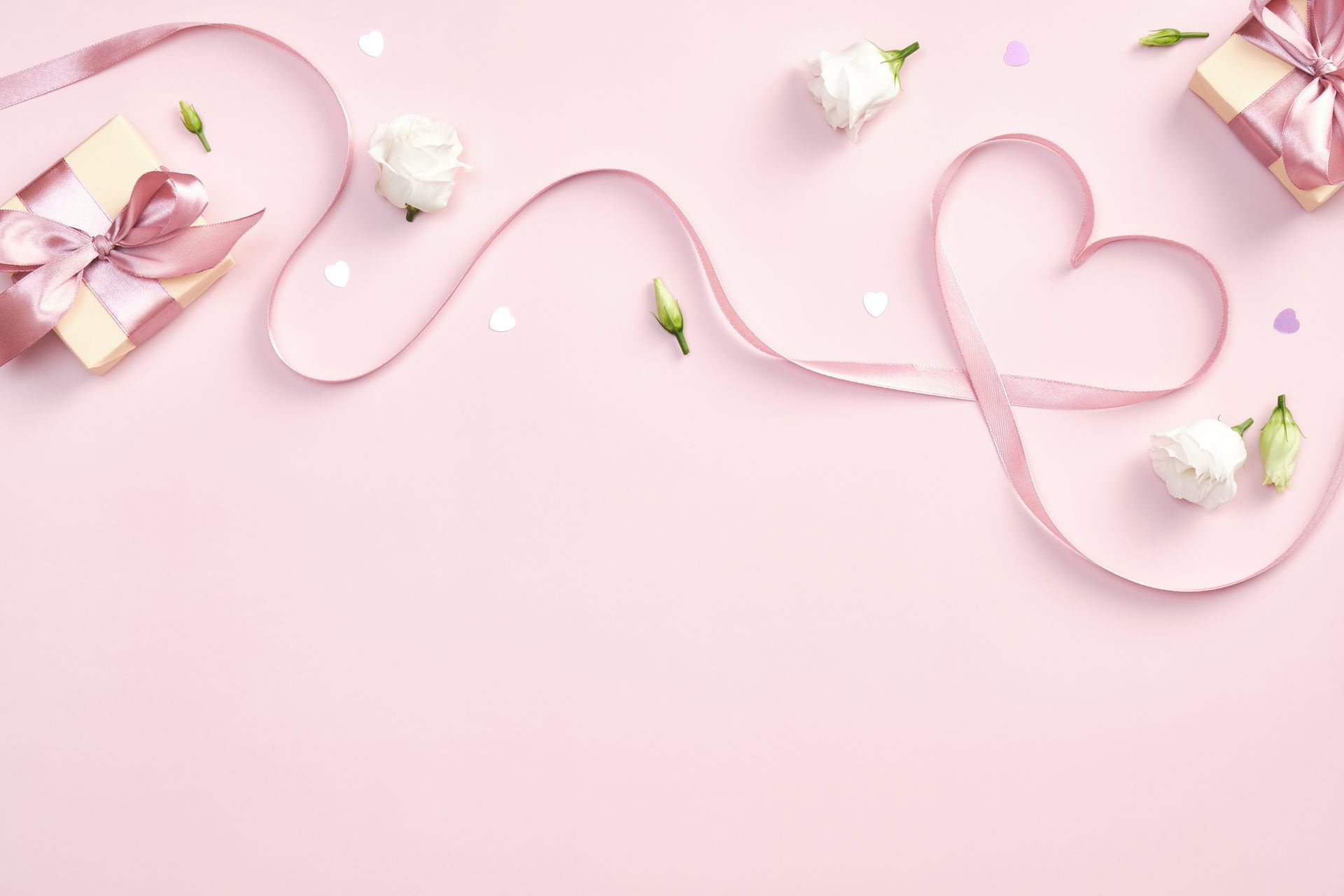 Fond rose avec des cadeaux, un ruban en forme de cœur, des fleurs et des confettis ; idéal pour la Saint-Valentin.