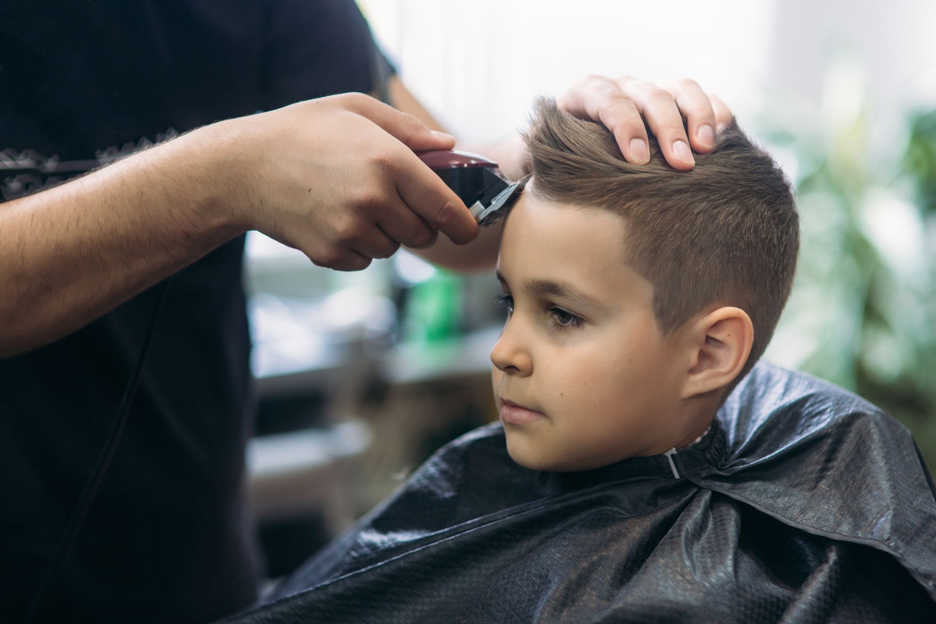 Garçon se faisant couper les cheveux dans un salon ; coiffeur utilisant une tondeuse sur ses cheveux ; expression concentrée.