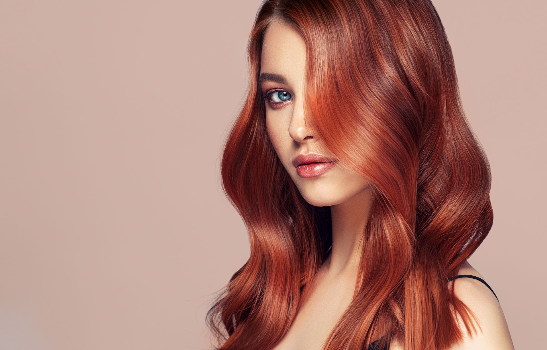Femme aux cheveux ondulés auburn, regardant vers la caméra, avec un arrière-plan neutre.