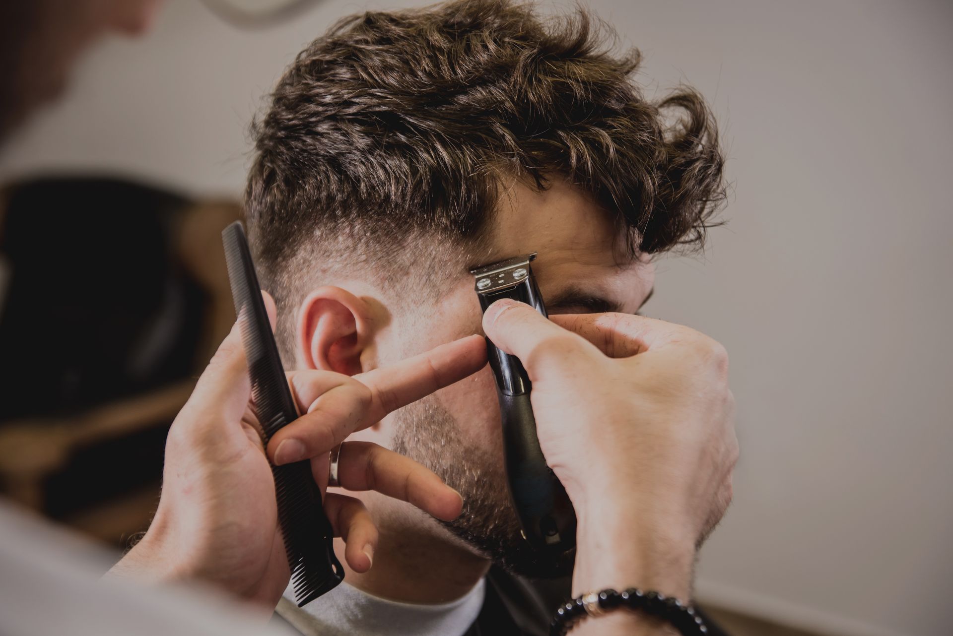 Un coiffeur coupe les cheveux d'un homme à la tondeuse. L'homme est dans un salon.