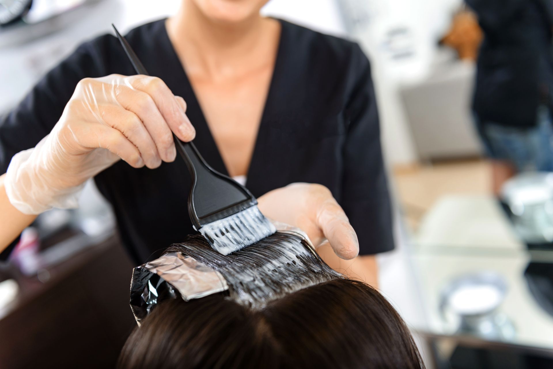 Coiffeur appliquant une teinture capillaire sur les cheveux d'un client avec une brosse dans un salon.