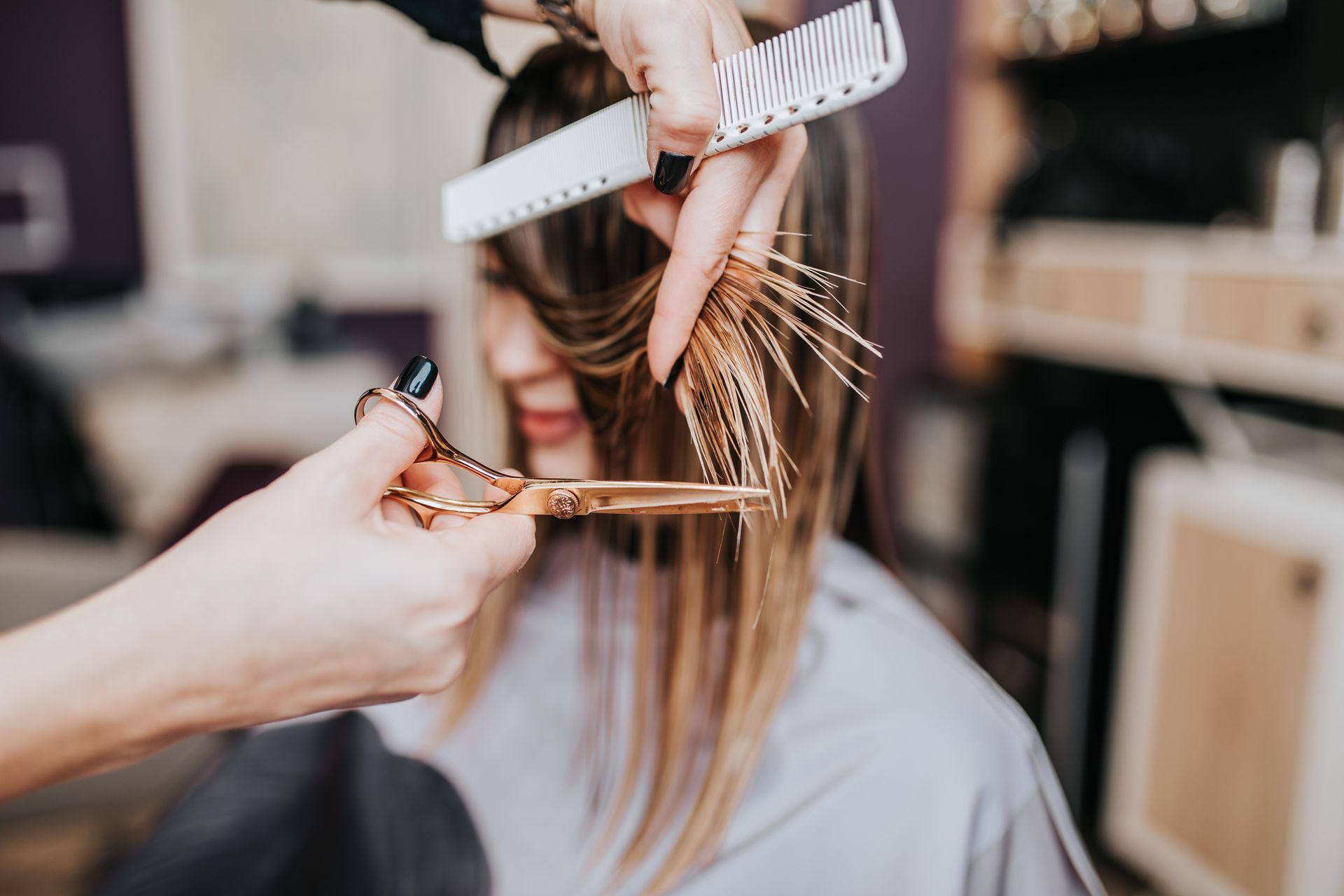 Un coiffeur coupe les cheveux d'une cliente avec des ciseaux et un peigne dans un salon. Gros plan avec des outils en or.