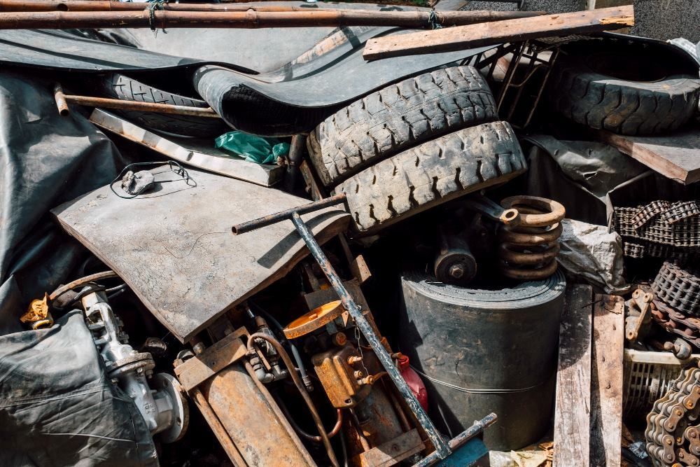Pile of scrap metal, including tires, wood, and a rusty machine, in an outdoor setting.