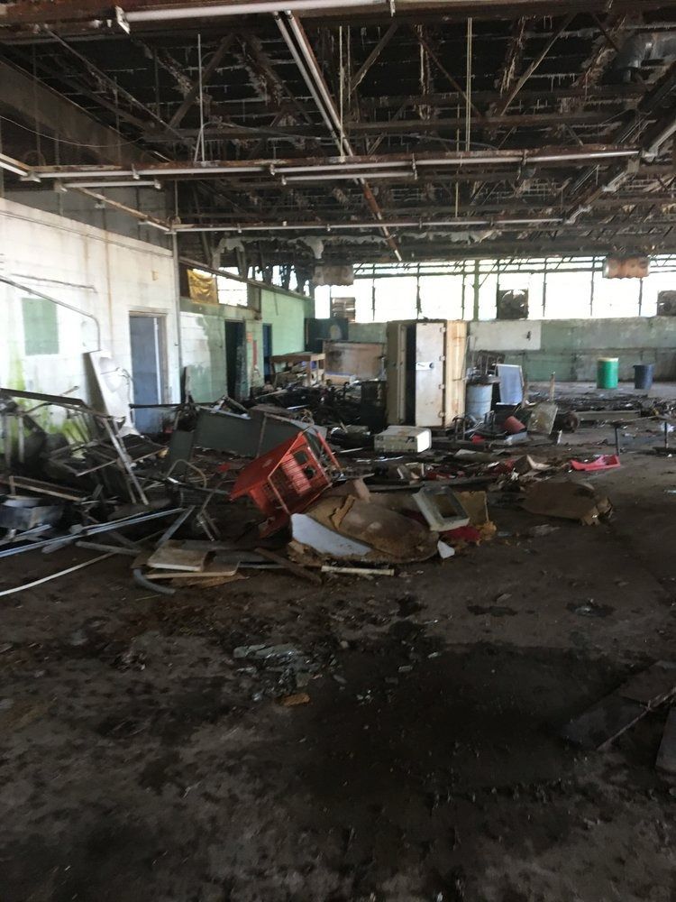 Interior view of a dilapidated, abandoned building. Debris and damaged equipment litter the floor.