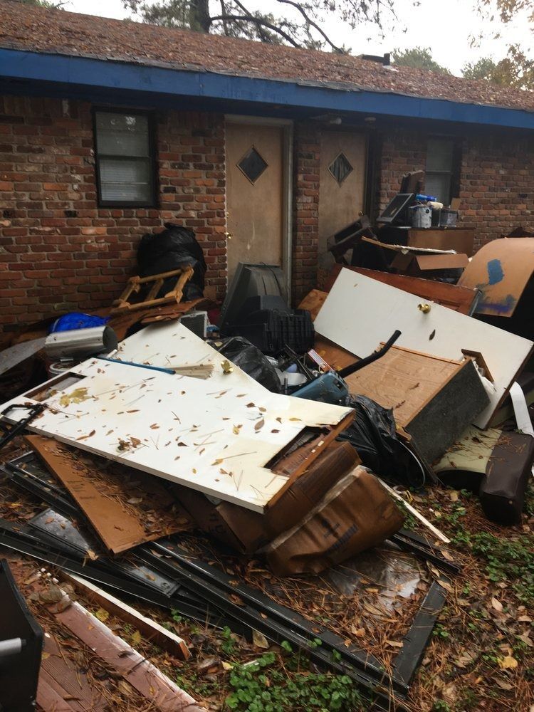 Exterior of a brick building with two doors. Debris, including wood and trash bags, is piled up near the doors.