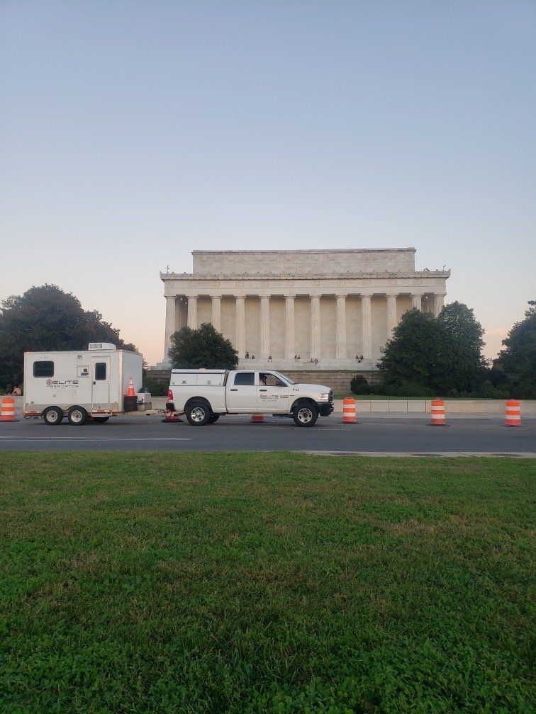 A truck with a trailer is driving down the road in front of the lincoln memorial.