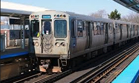 A subway train is pulling into a station on a sunny day.