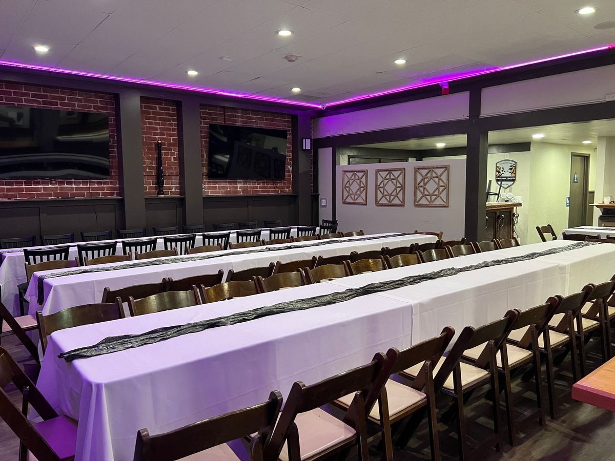 A long table and chairs in a room with purple lights.