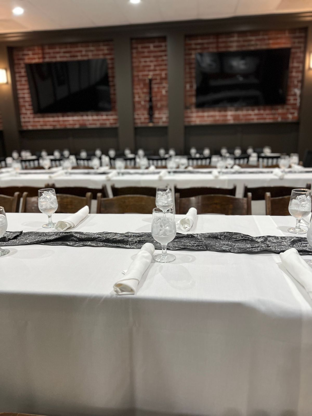 A long table with a white table cloth and glasses on it in a room.