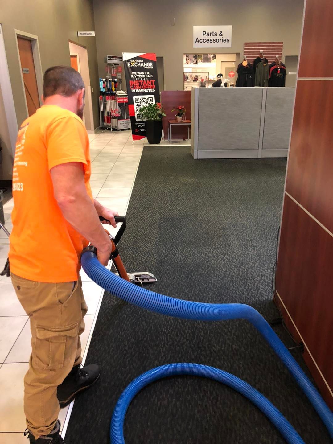 Man wearing an orange shirt using a vacuum cleaner to clean carpeted flooring in a Cleveland‑area home.