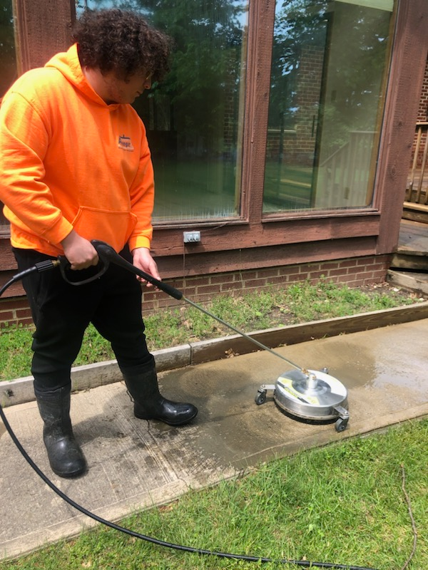 Local Cleveland cleaning professional in an orange hoodie pressure washing a sidewalk.
