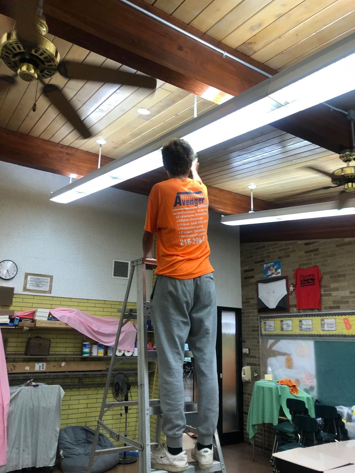Man on a ladder wearing an orange shirt that says 