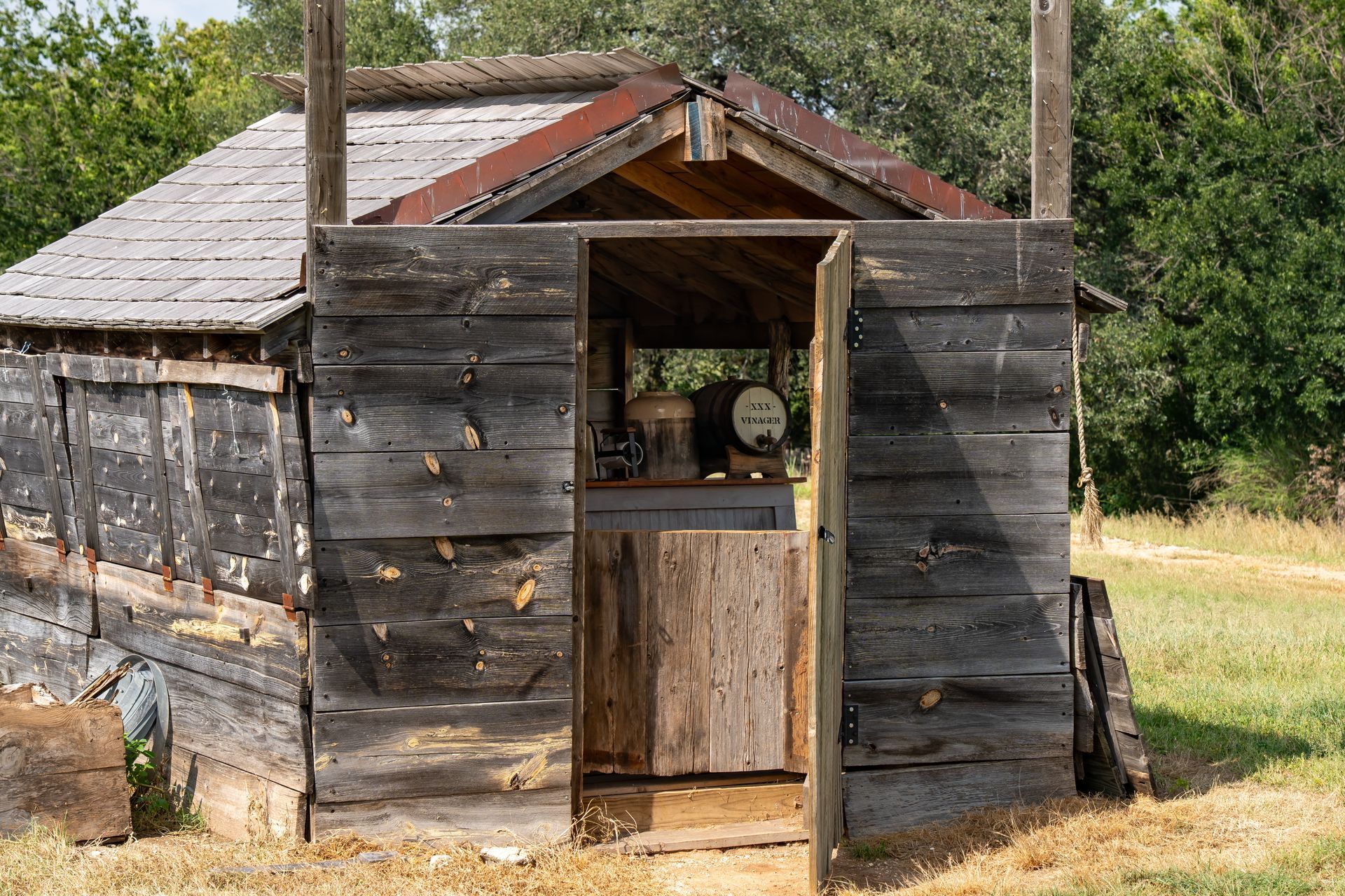 Weathered wooden shed with open doorway and corrugated roof in a grassy rural setting
